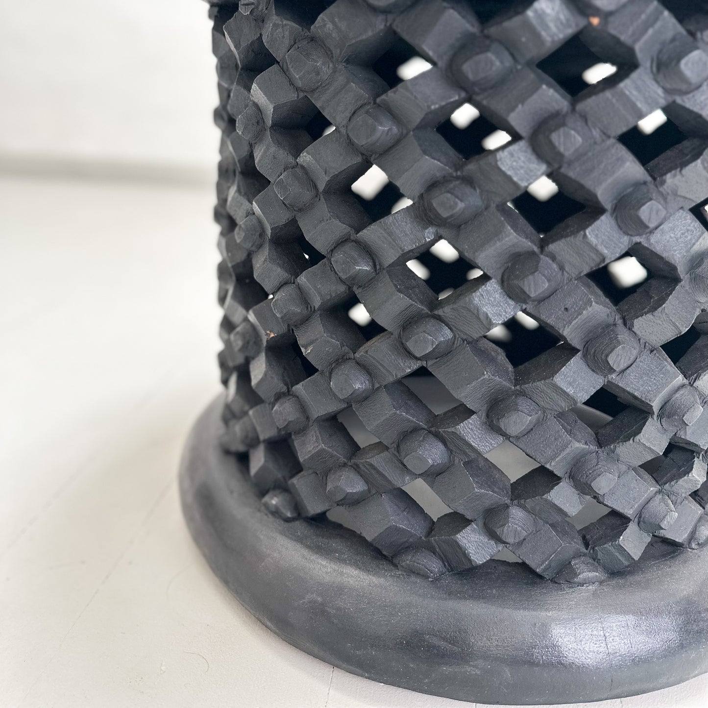 A Bamileke stool with crosshatch engraved sides and a solid color top, predominantly in black.