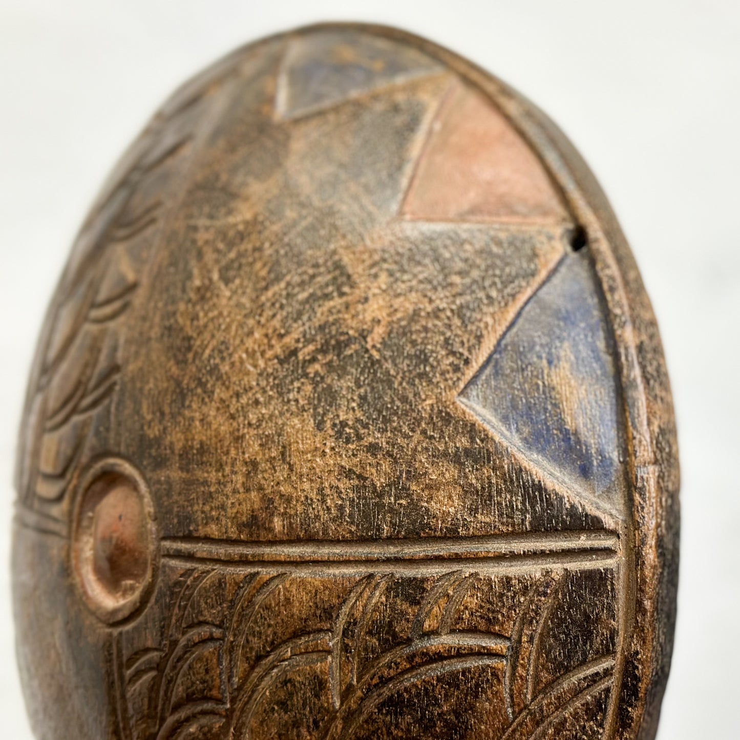 A carved wooden shield with geometric patterns displayed on a stand against a white background.