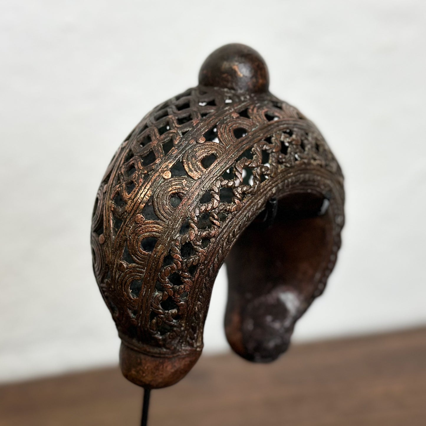 Three bronze anklets with intricate geometric patterns displayed on individual stands against a white background.