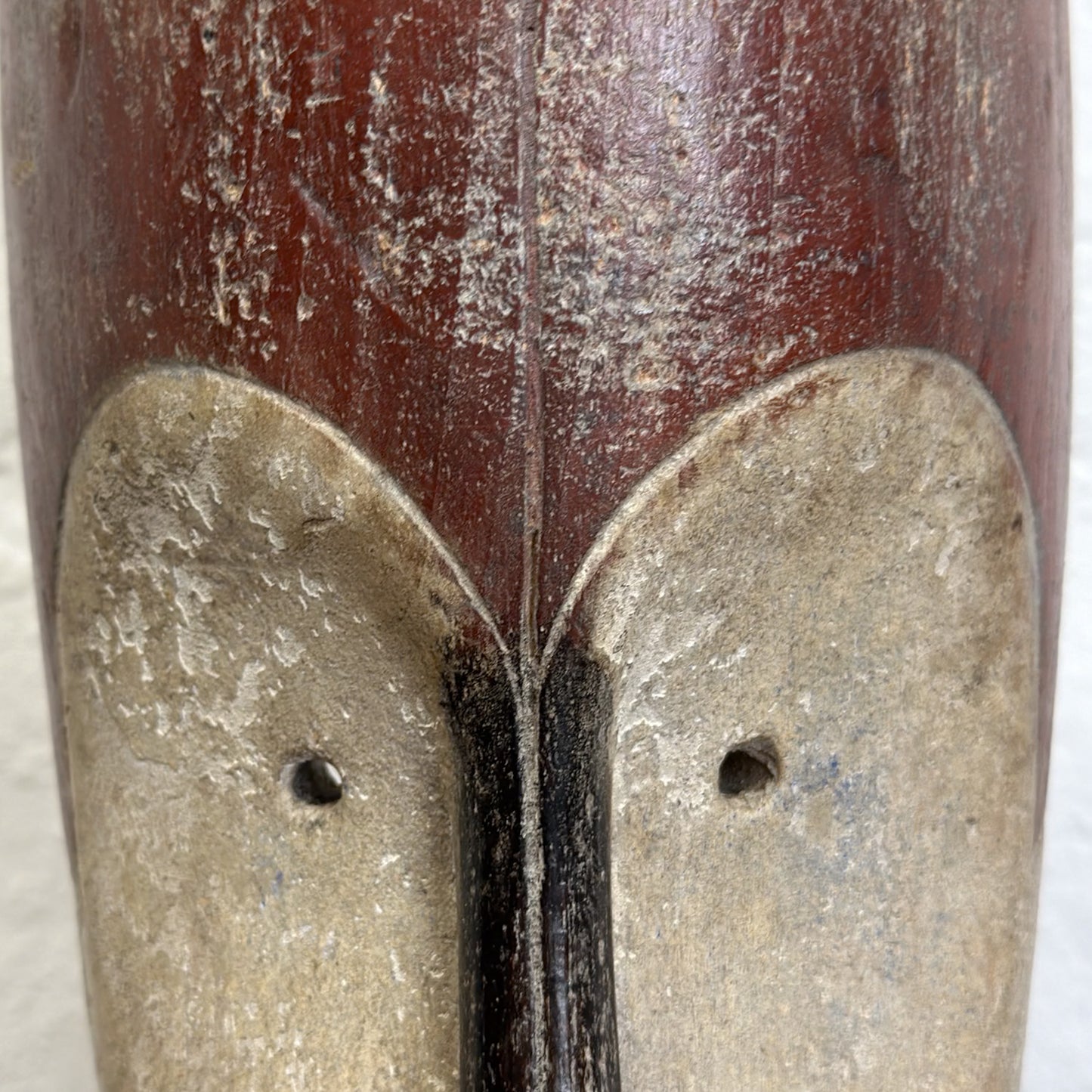 A wooden decorative mask with geometric patterns, mounted on a metal stand.