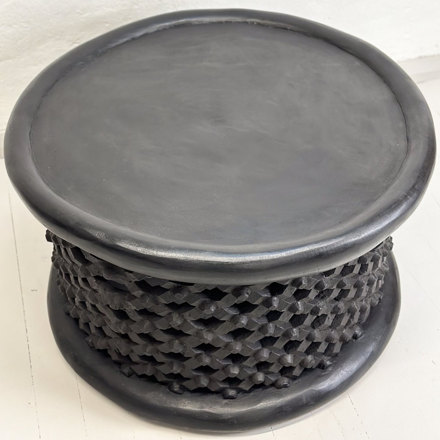 A black Bamileke coffee table with a geometric pattern, likely made of wood, against a white background.