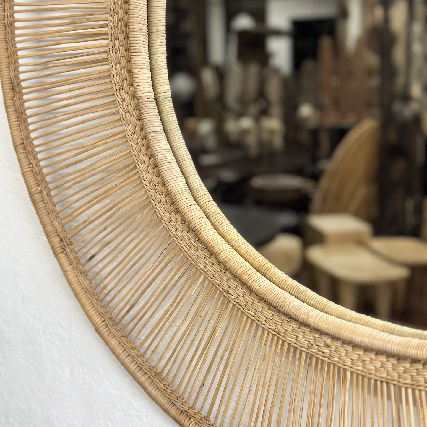 A round mirror with a natural beige straw frame, hanging on a wall.