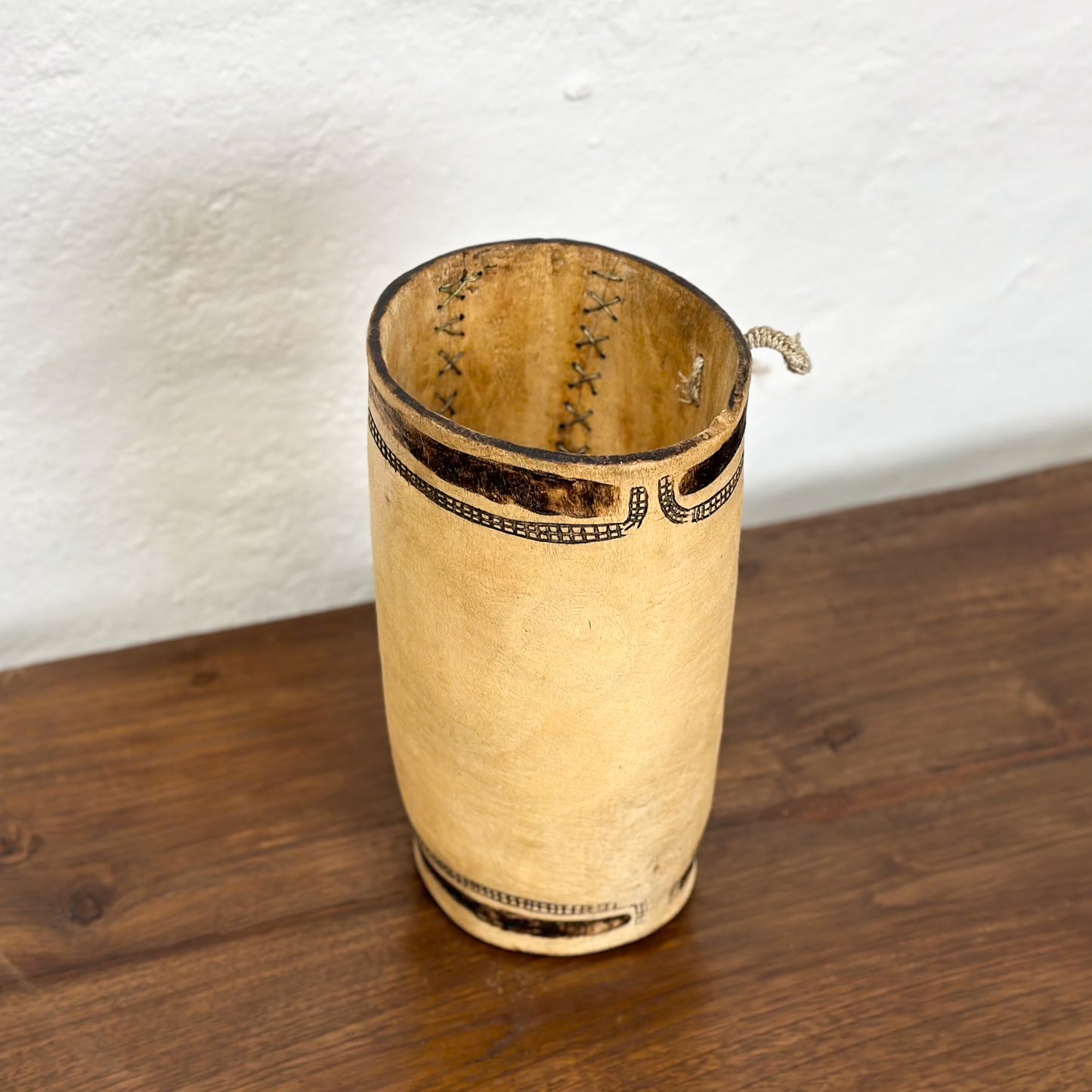 A beige-colored, textured wooden container with stitched joins and geometric line patterns, placed against a plain background.