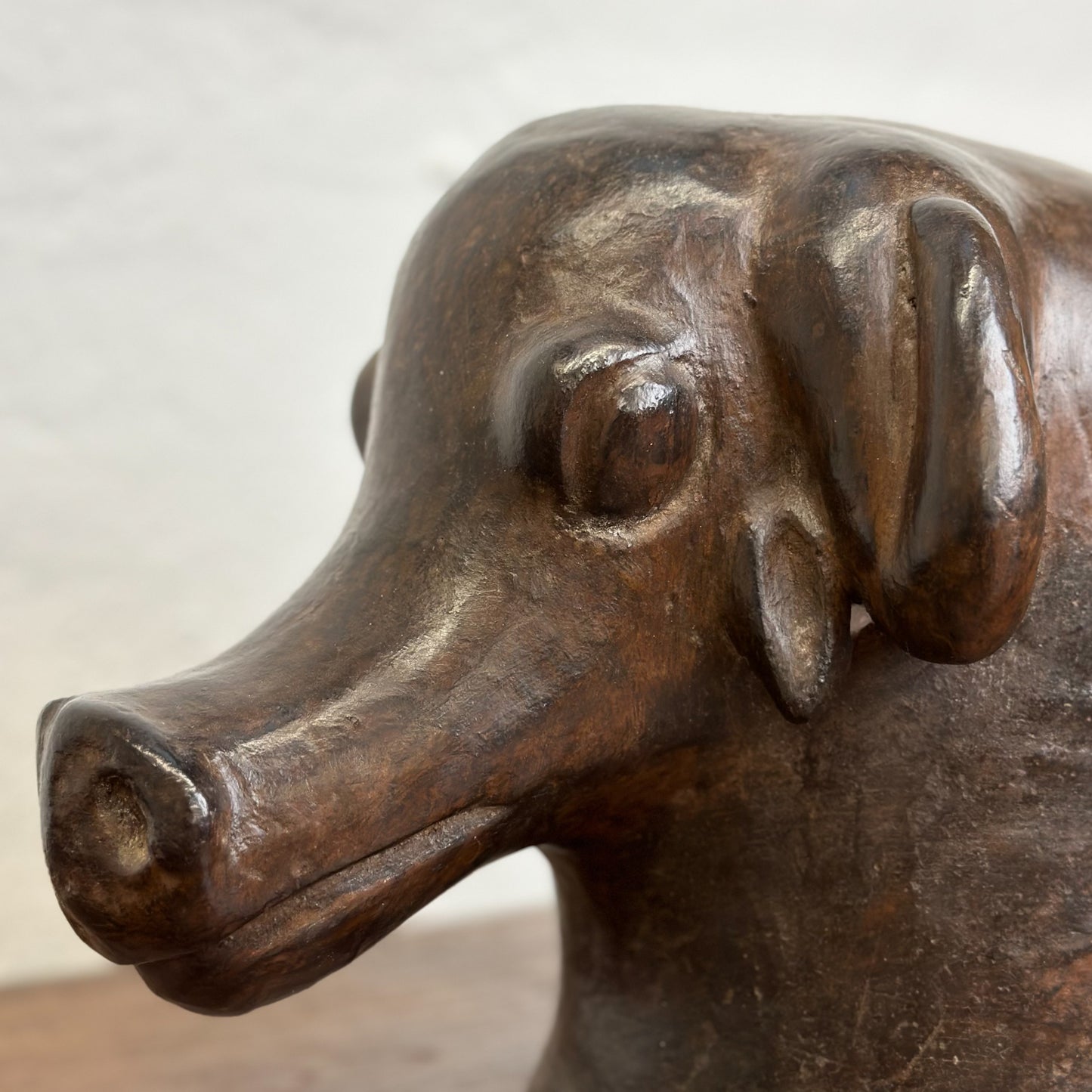 A sculpted clay animal helmet resembling a dog's head, placed on a wooden surface against a white wall.