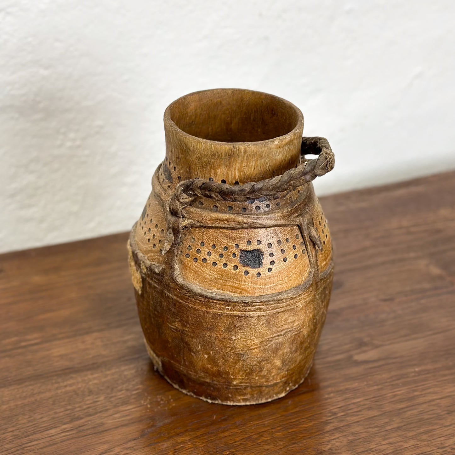 A traditional, handcrafted ceramic vase with a beige and brown color, featuring hole patterns and a rope tied around it.