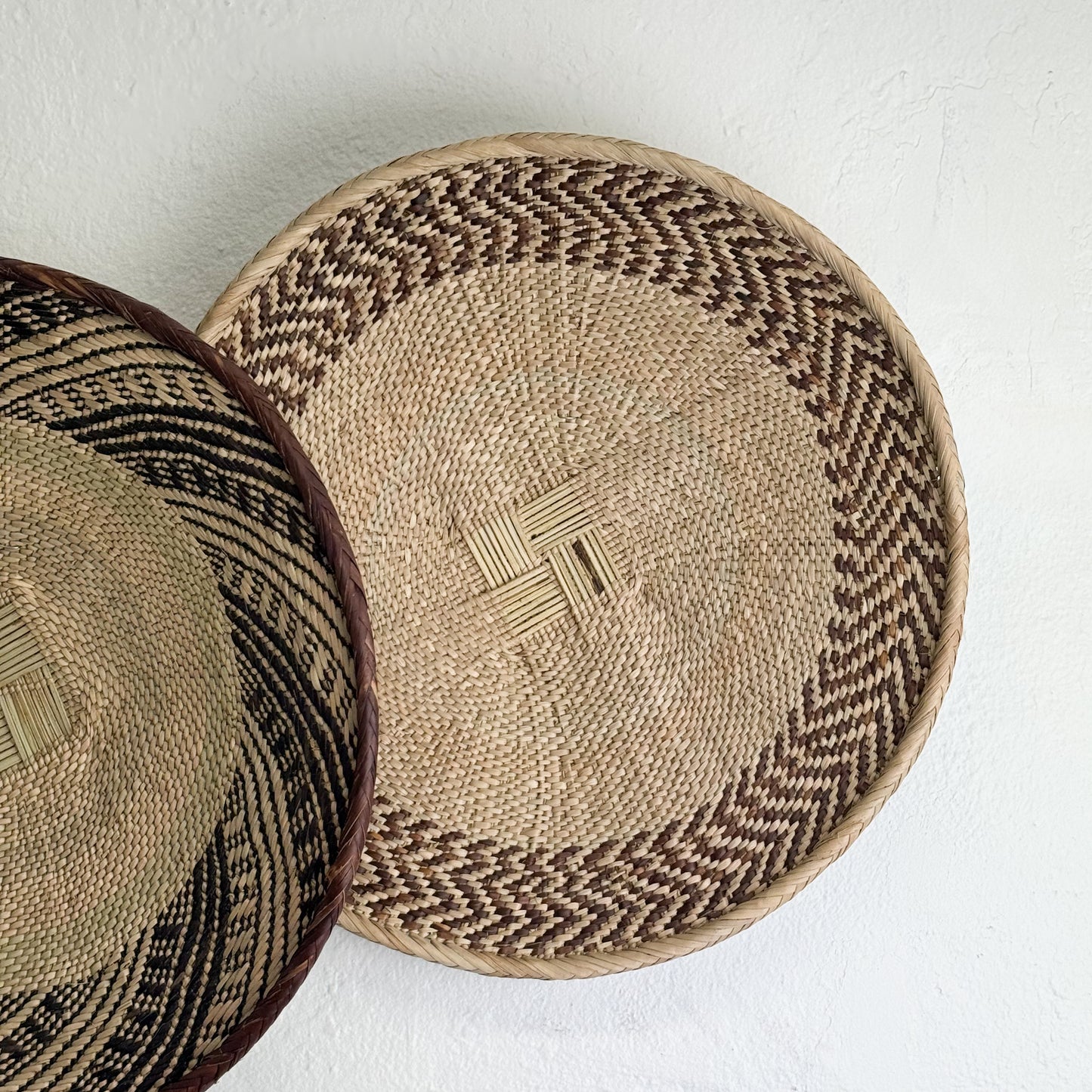 Two woven baskets with geometric patterns on a white background