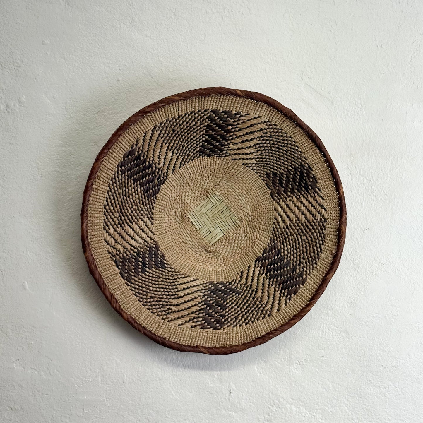 Round woven basket with a geometric pattern on a white background