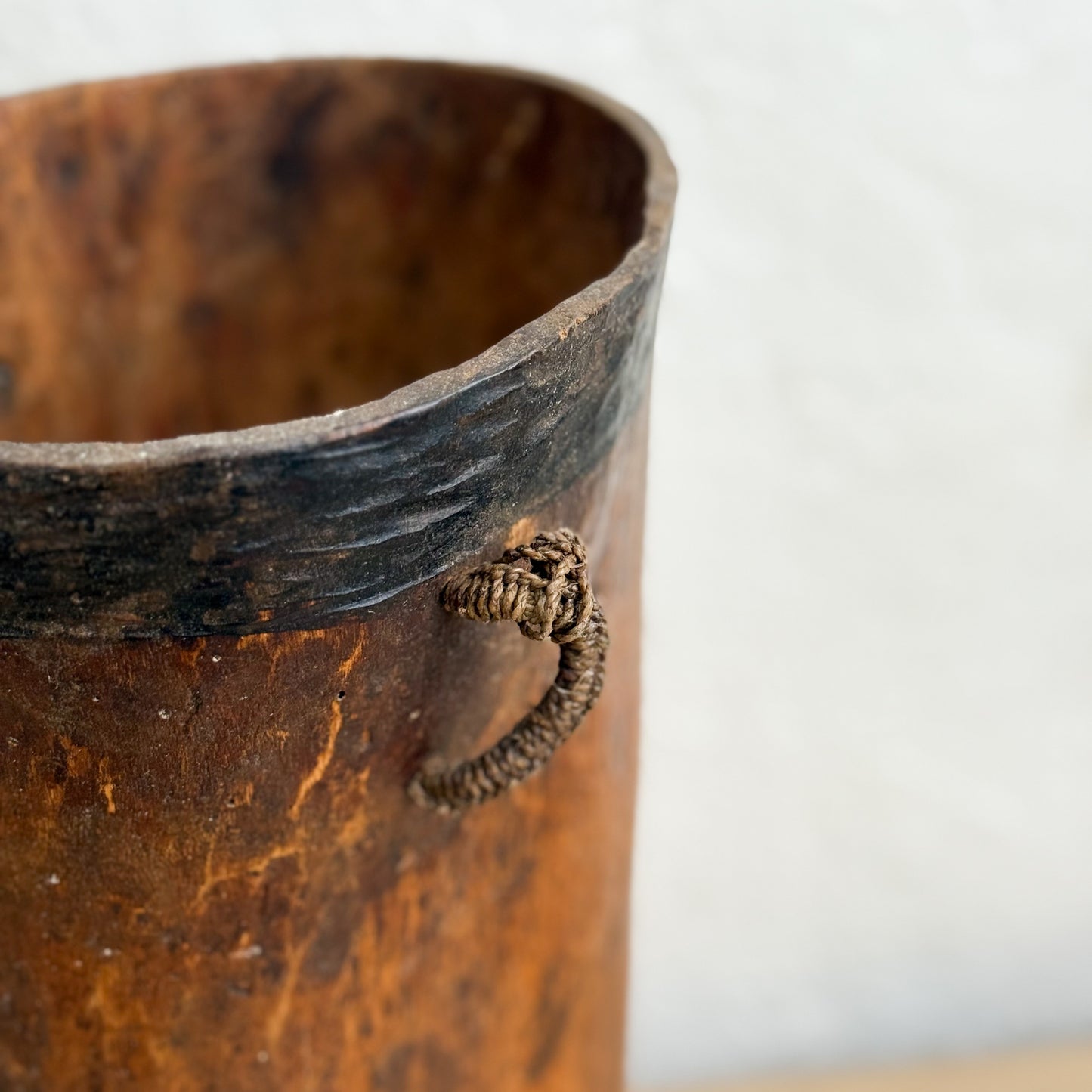 Close-up of a rustic wooden vase with a textured surface and a small decorative element on a white background.