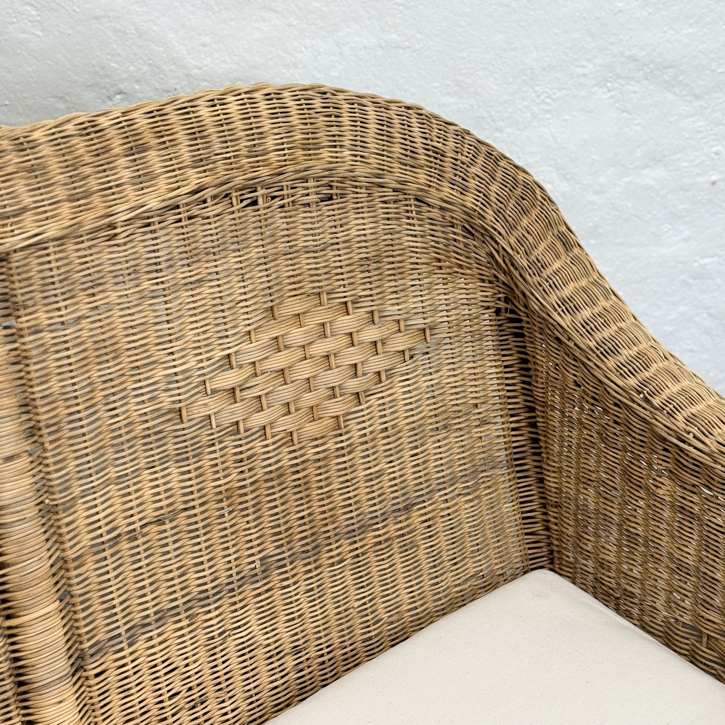 Wicker chair corner with a white cushion on a light gray background