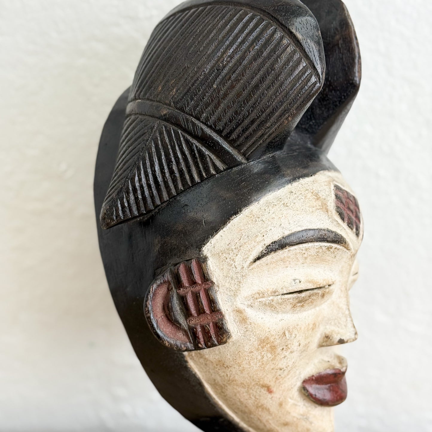 Carved wooden mask with black and beige details on a white background