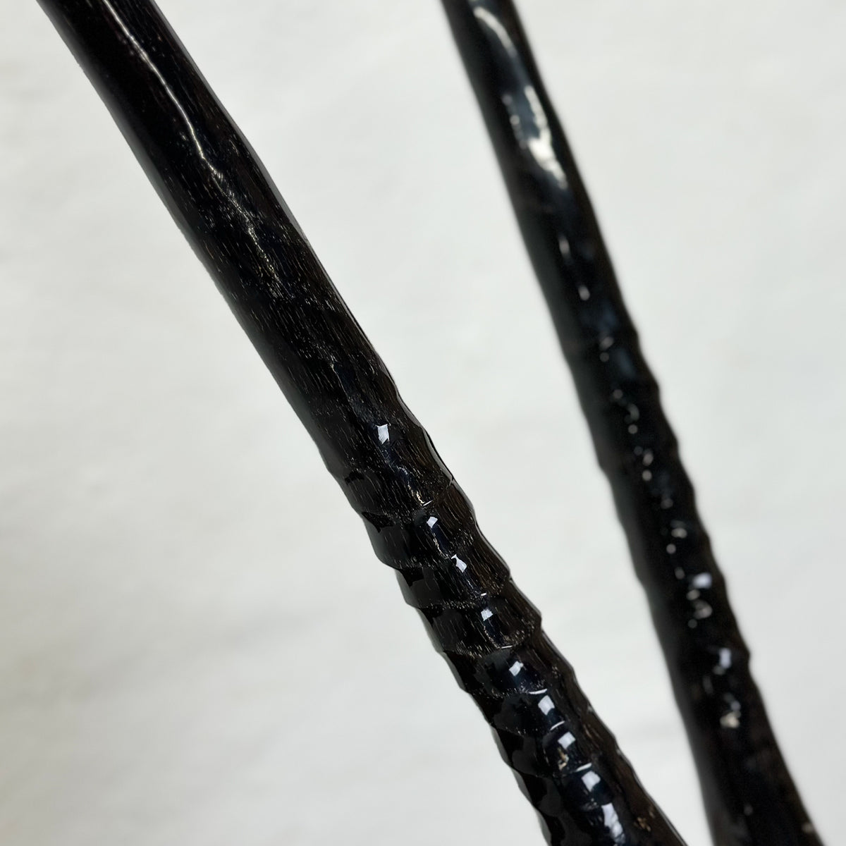 Close-up of two glossy black textured rods or handles against a light gray background.