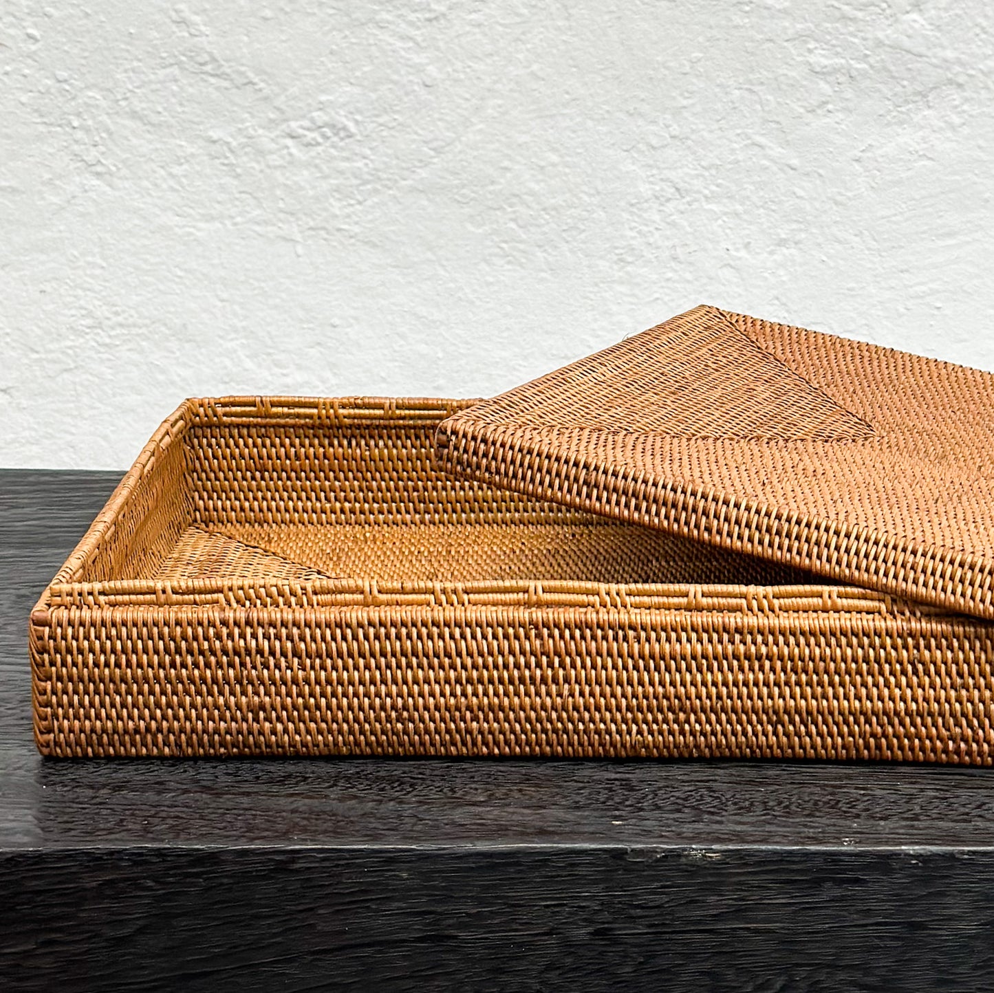 A rectangular atta basket box with lid, woven from wheat straw, placed on a dark surface with a plain wall in the background.
