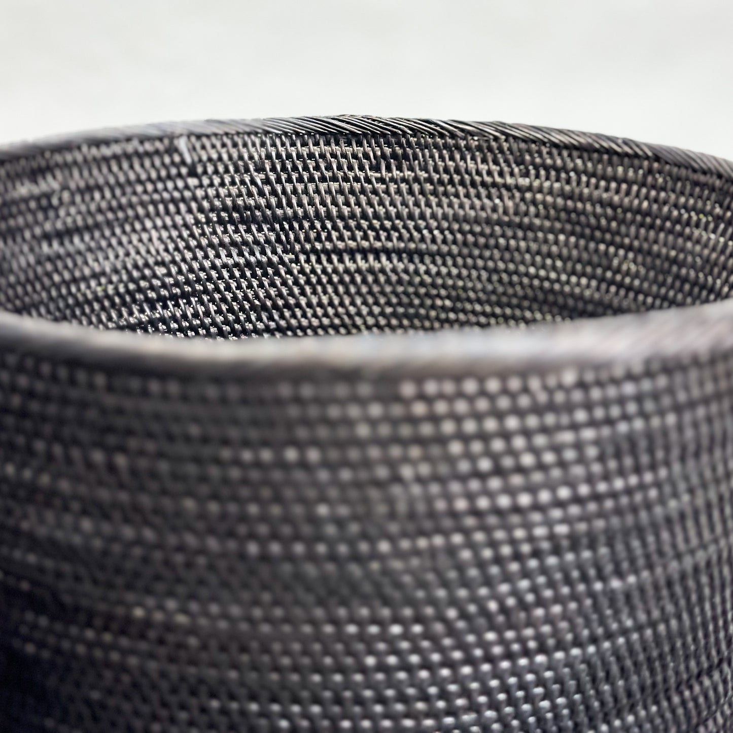 Two black tapered dustbins with a woven texture, placed on a dark surface.