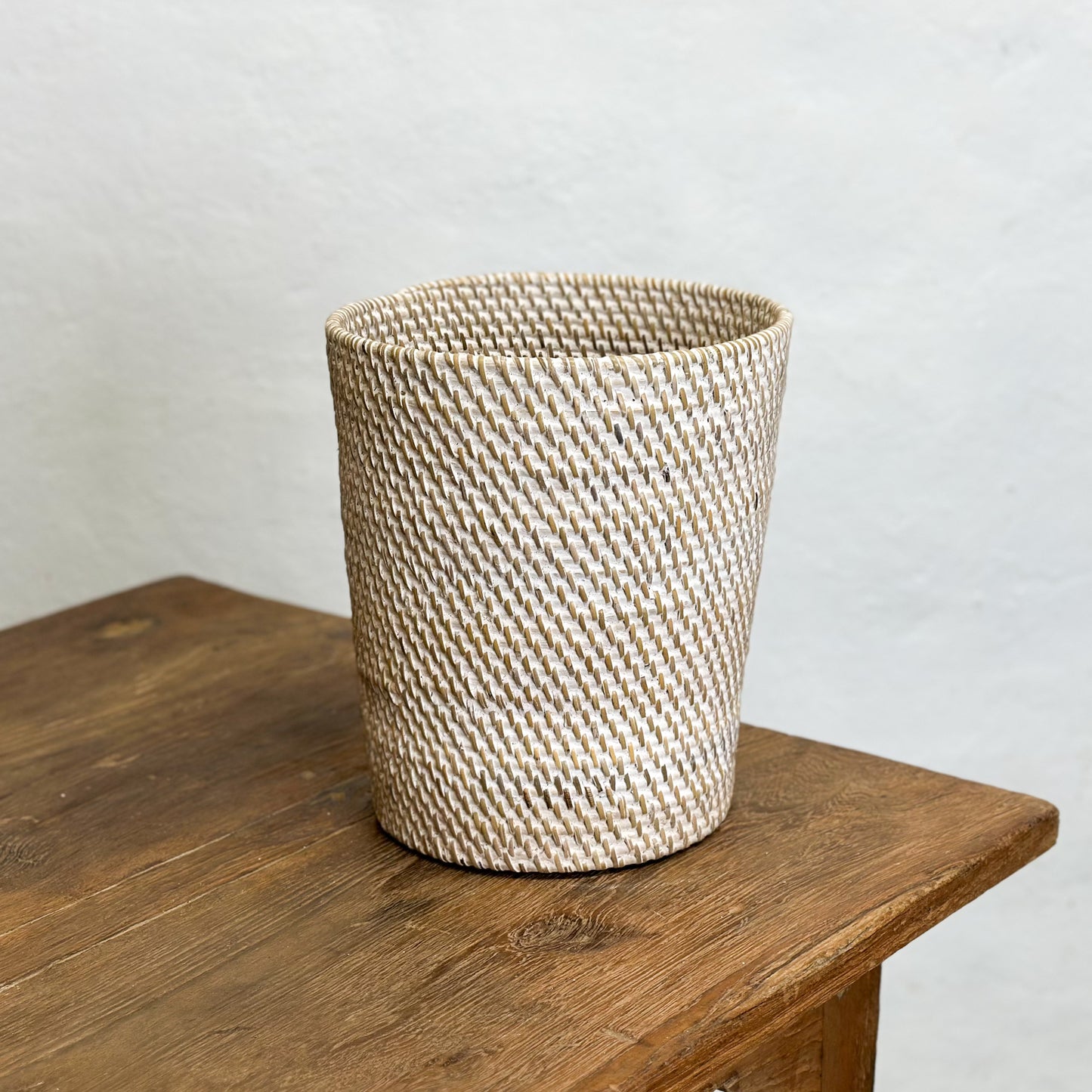Three tapered rattan waste paper baskets in beige, brown, and black colors, displayed on a wooden table.