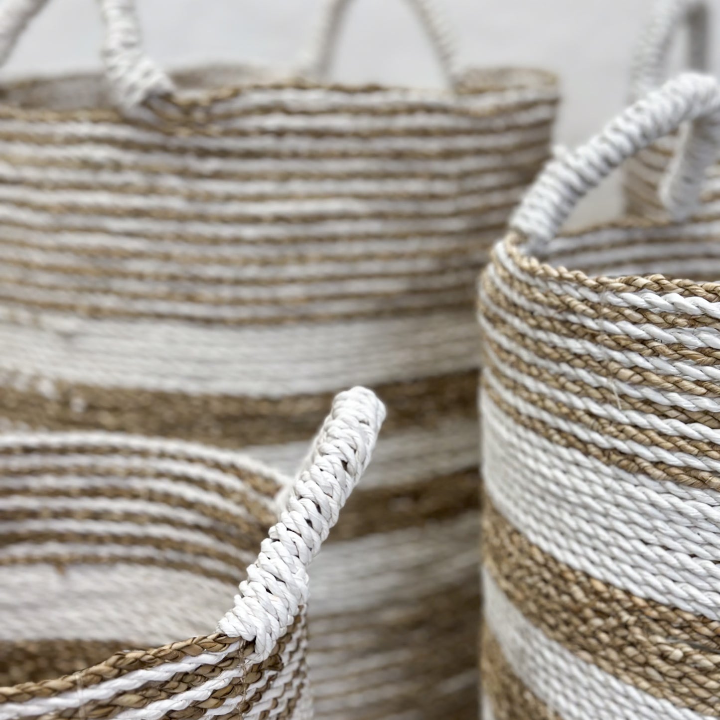 A collection of candy stripe sea grass baskets in various sizes displayed on a floor against a wall, with natural lighting.