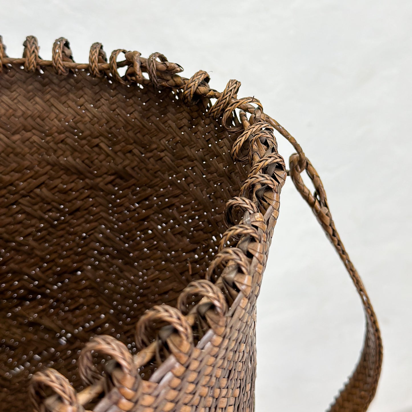 A brown woven basket with geometric patterns, displayed on a wooden surface.