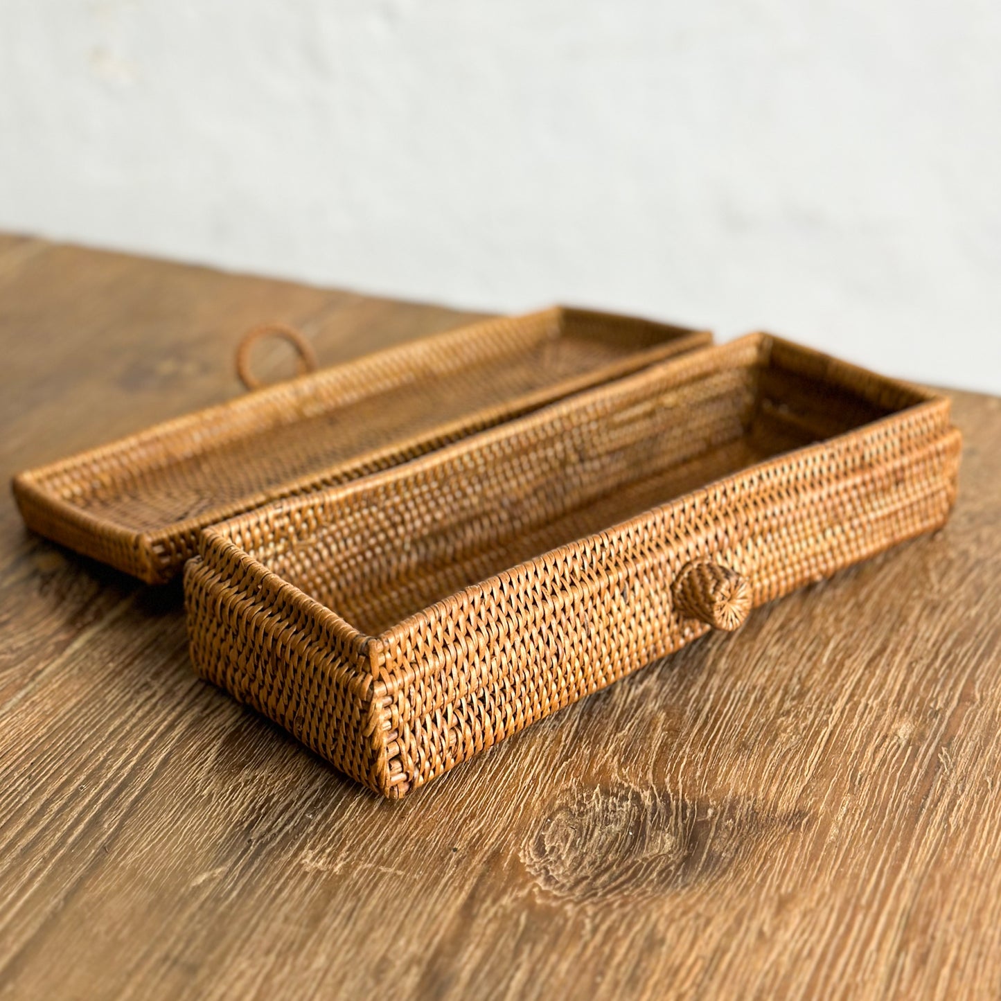 A wicker pencil box with a bow detail on a wooden surface with a plain background.