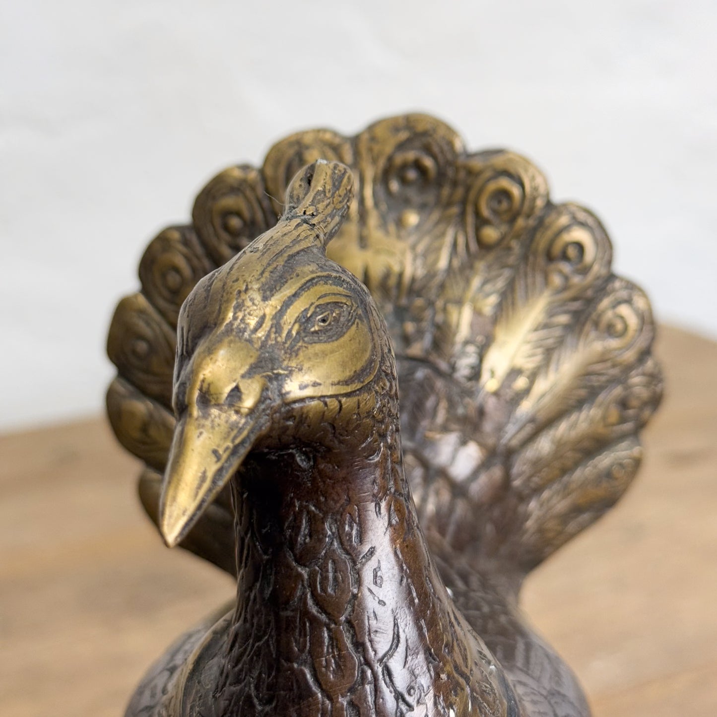 A bronze sculpture of a peacock standing on one leg, with intricate patterns and a glossy finish.