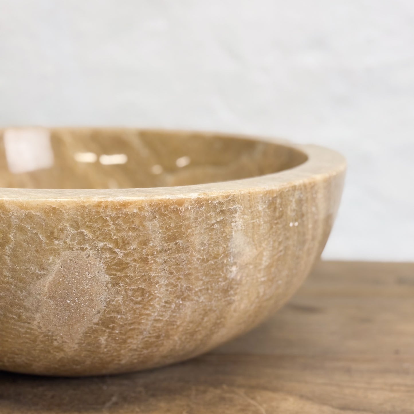 A beige onyx stone basin with a smooth finish, displayed on a wooden surface against a white background.
