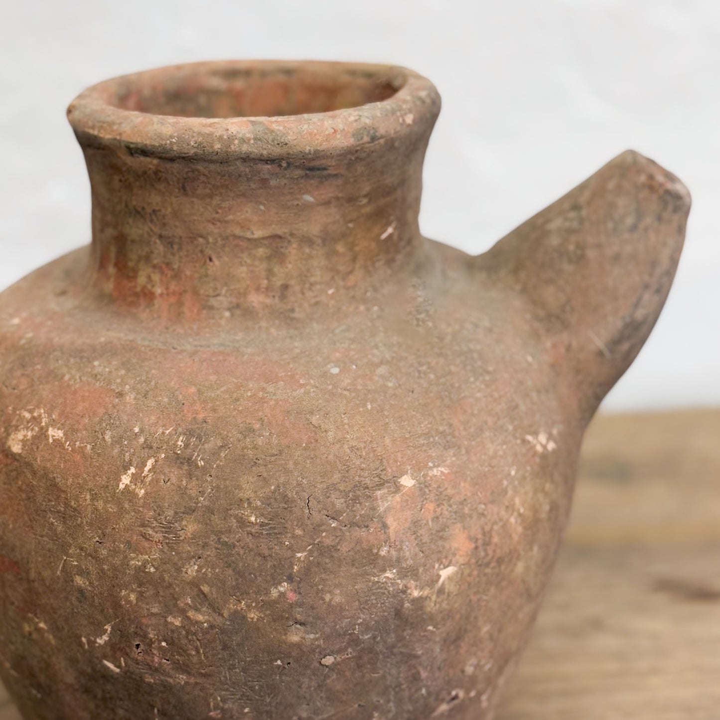 A brown terracotta pot with a spout, handmade, displayed on a wooden surface.