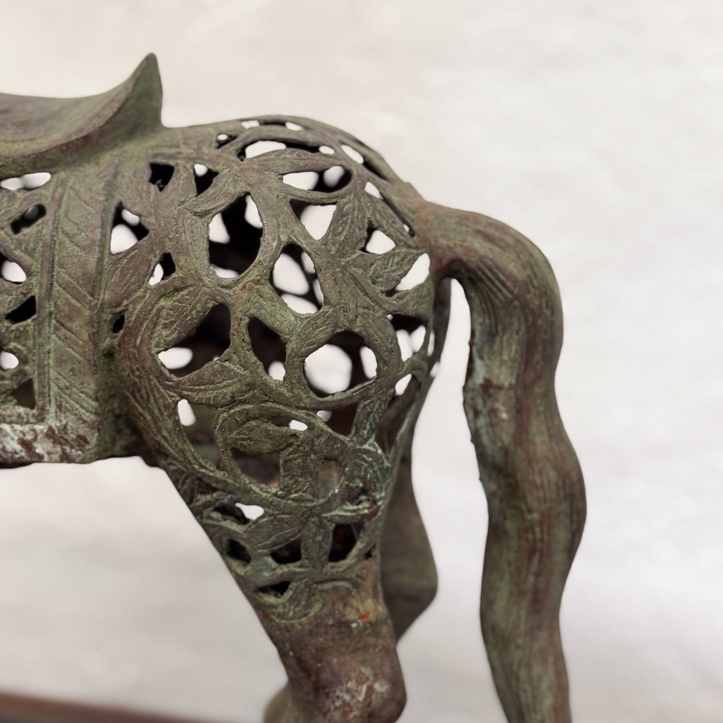 A bronze filigree horse statue with intricate cut-out patterns, placed on a black base.