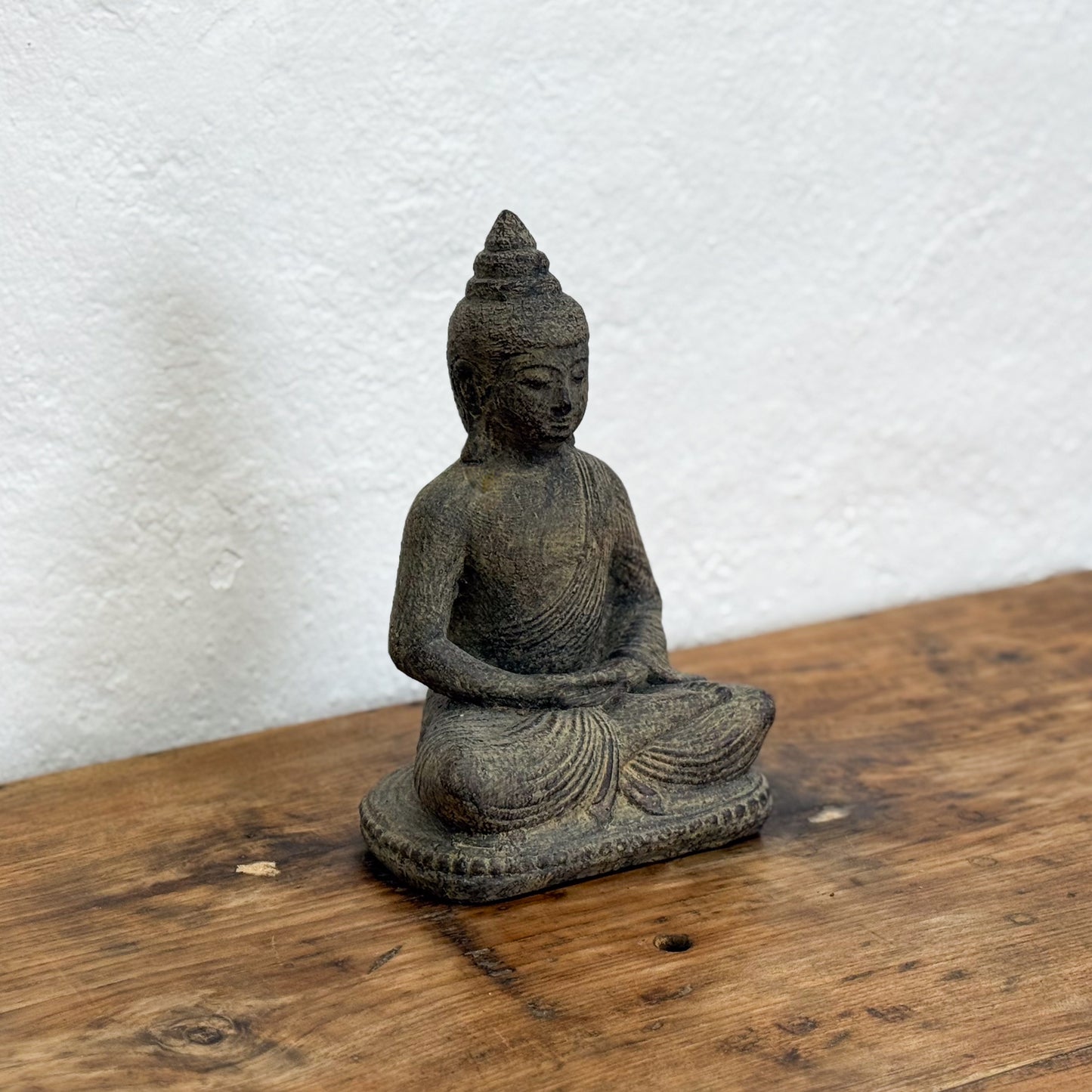 Statue of a meditating Buddha on a wooden surface with a white textured wall background