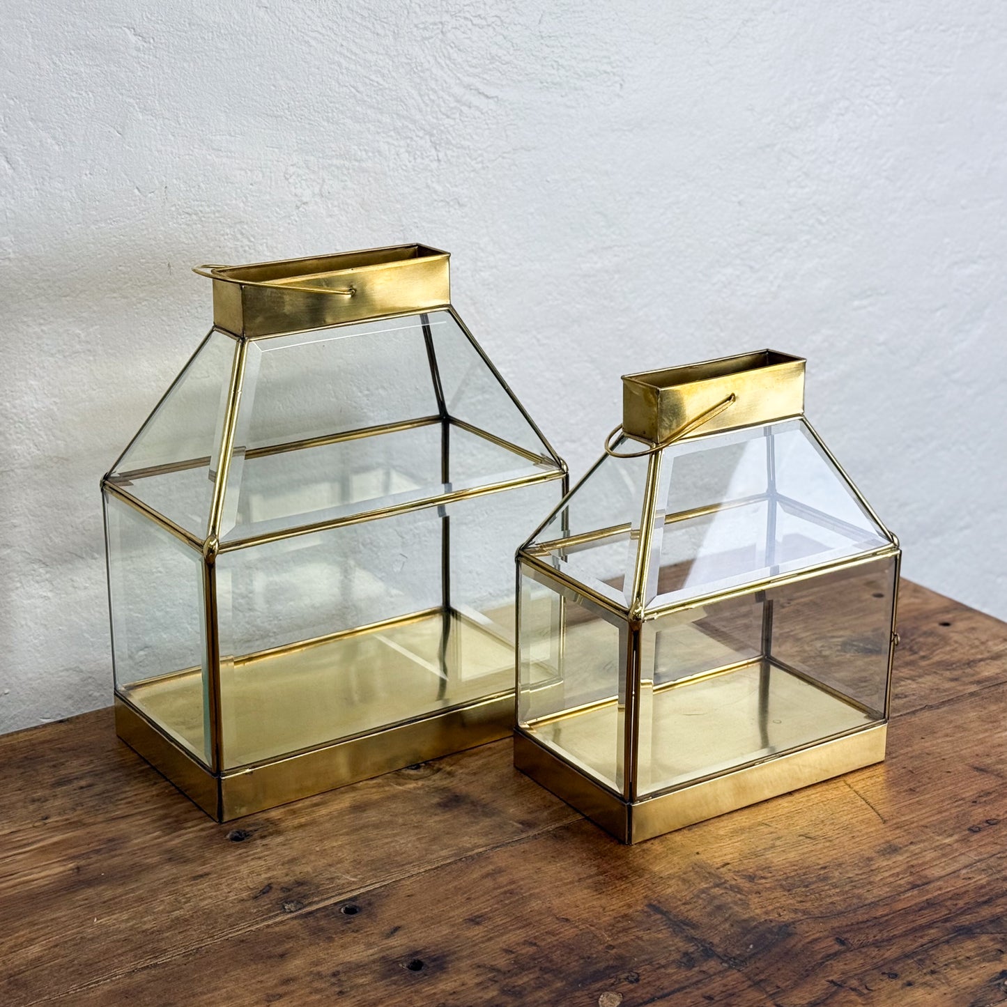 Two gold-framed glass lanterns on a wooden surface with a white wall background.