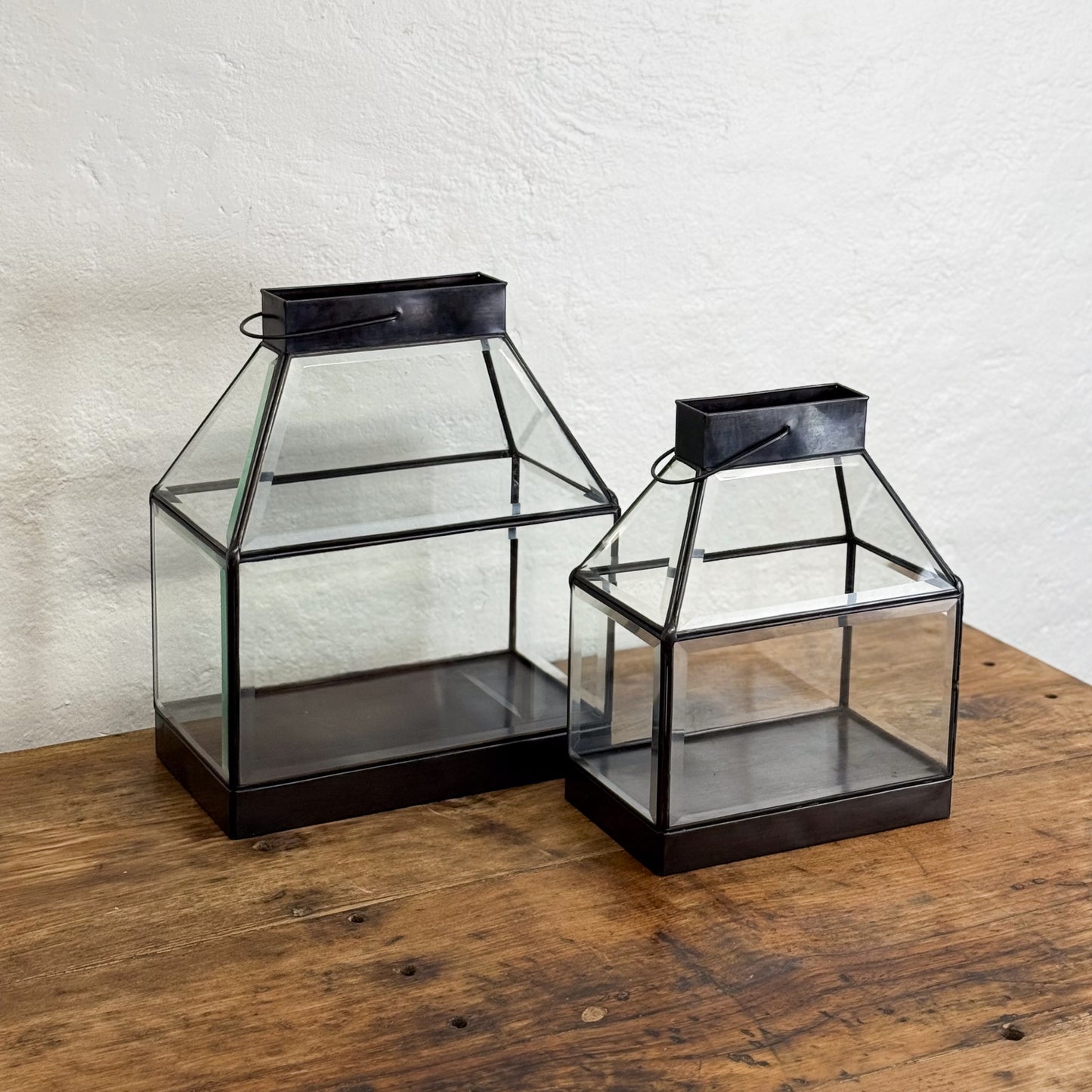 Two glass lanterns with black metal frames on a wooden surface.
