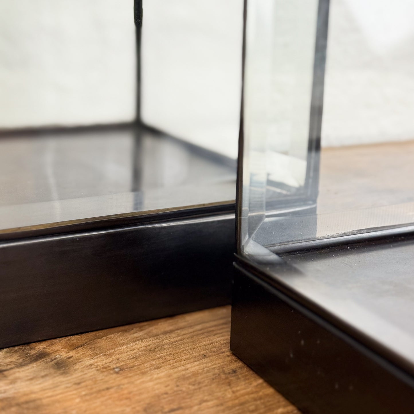 Close-up of a glass display case corner on a wooden floor.