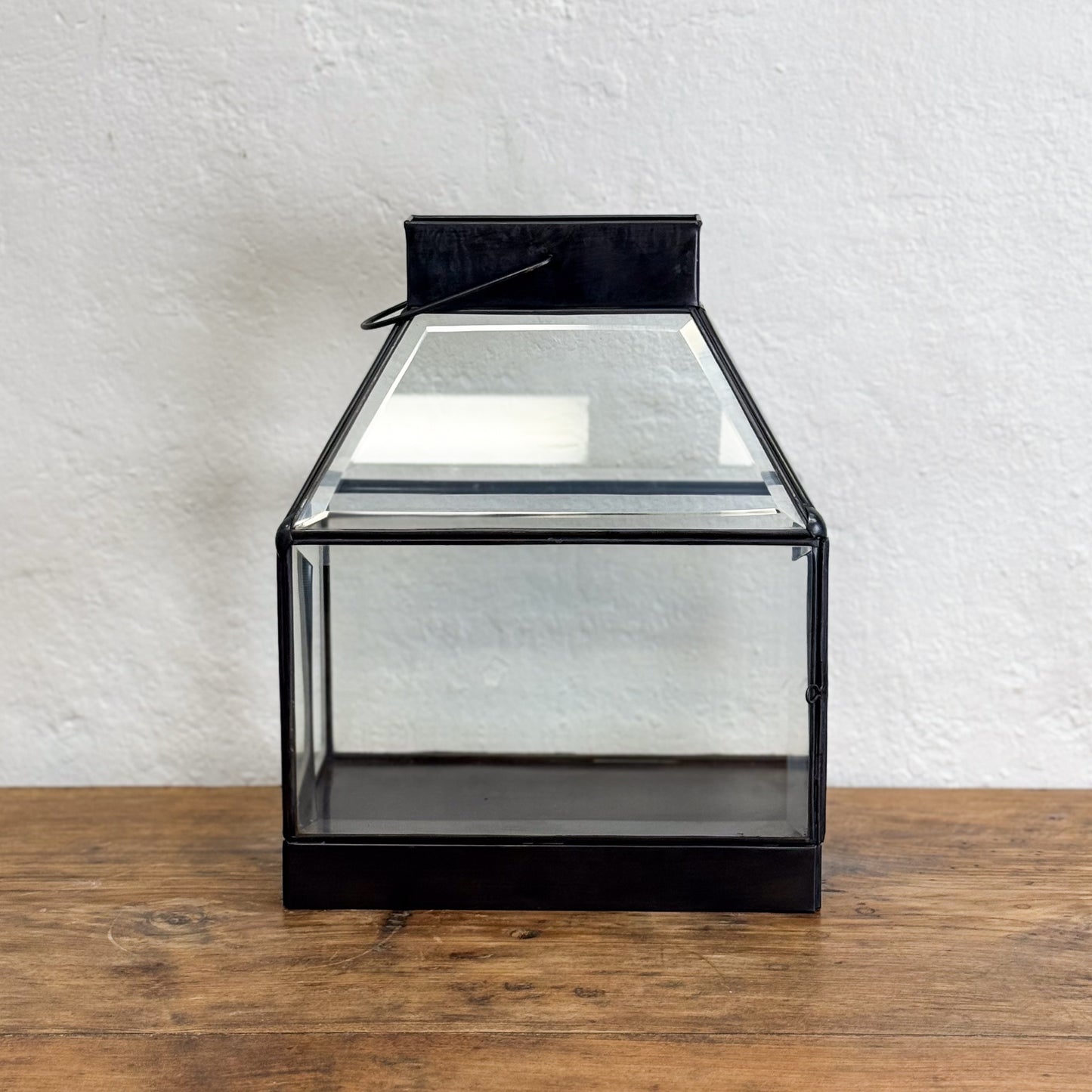 Black glass lantern on a wooden surface with a white textured wall background