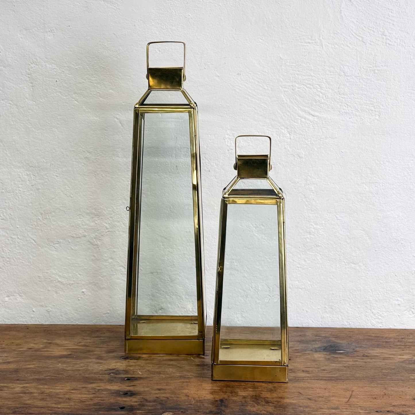 Two gold lanterns on a wooden surface with a white textured wall background