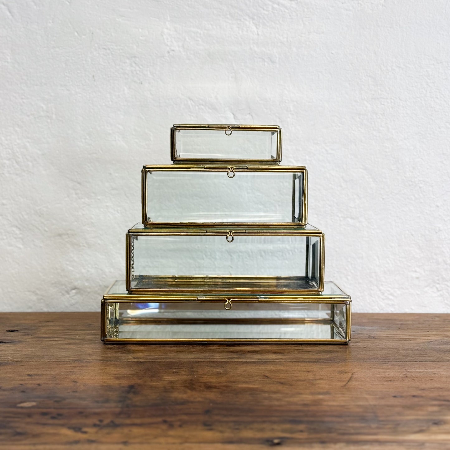 Set of three nested glass boxes with gold trim on a wooden surface and white textured wall background
