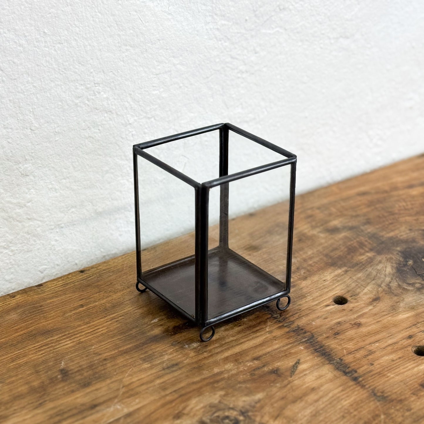 Small black metal shelf on a wooden surface with a white textured wall background