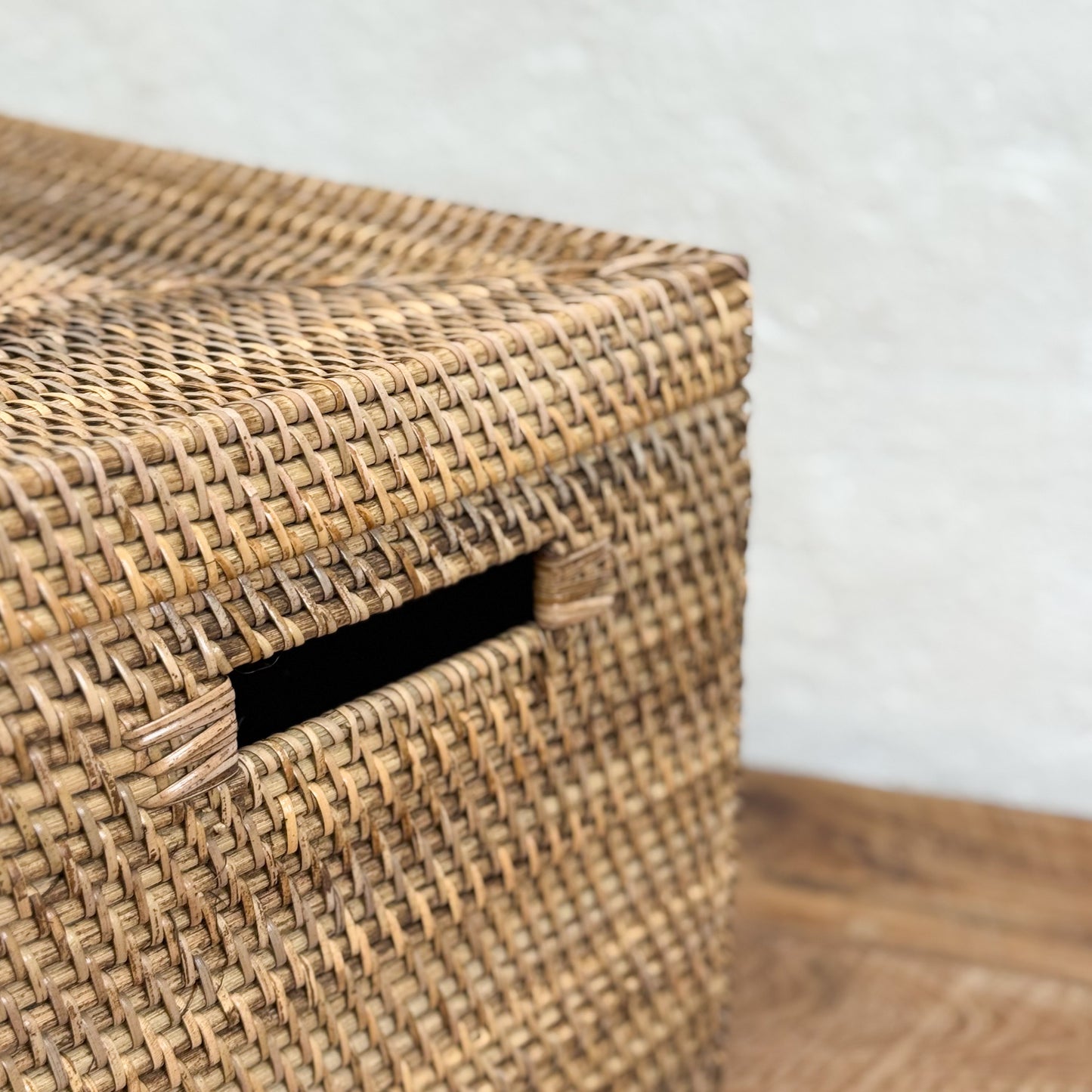 Woven basket with a lid on a wooden floor against a white wall