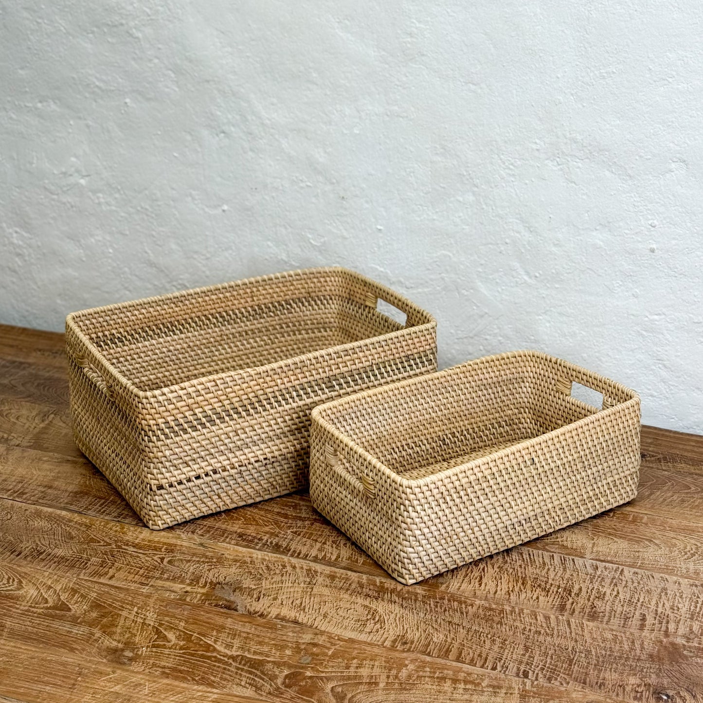 Two woven baskets on a wooden surface with a gray wall background