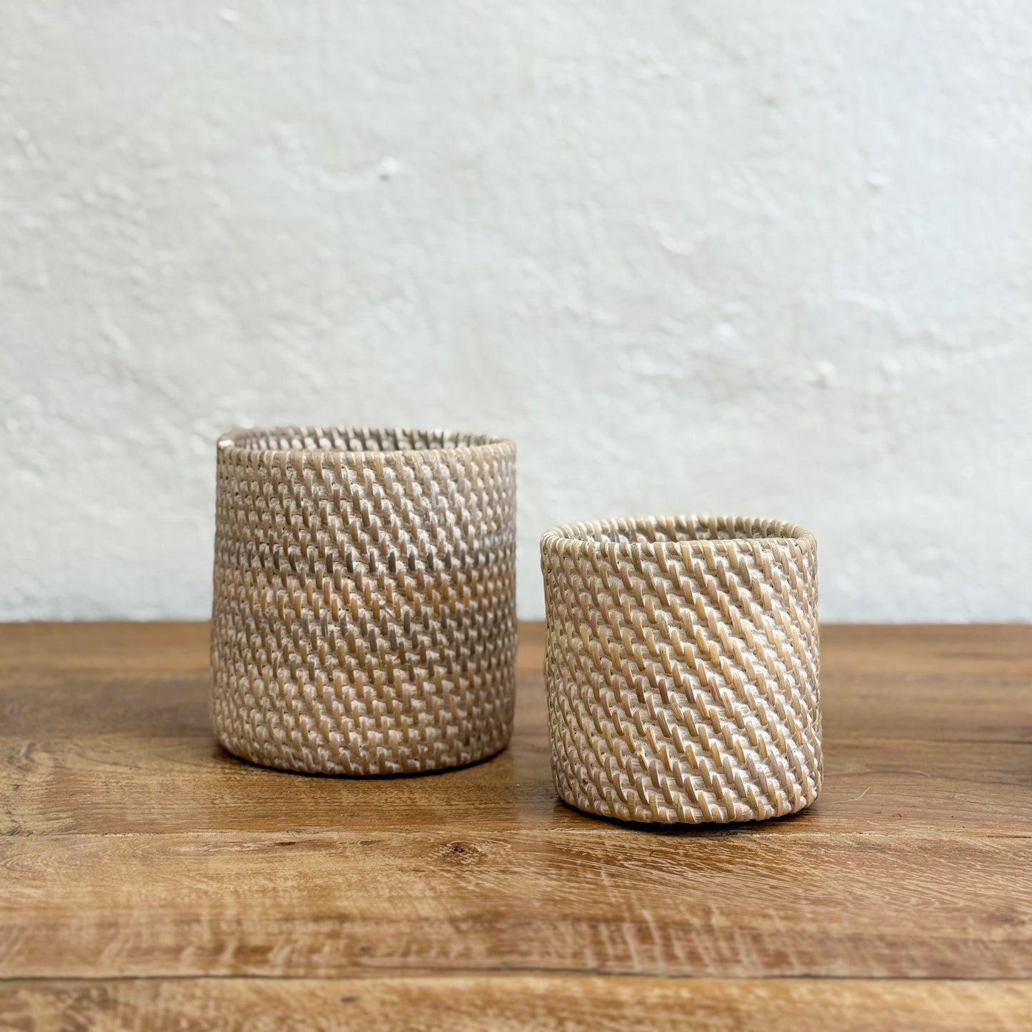 Two woven baskets on a wooden surface with a textured wall background