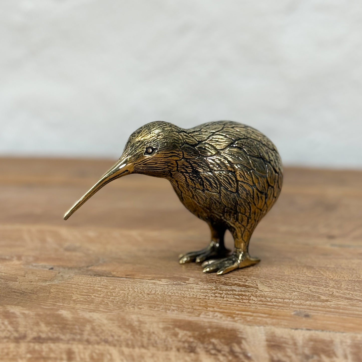 Bronze kiwi bird figurine on a wooden surface with a neutral background