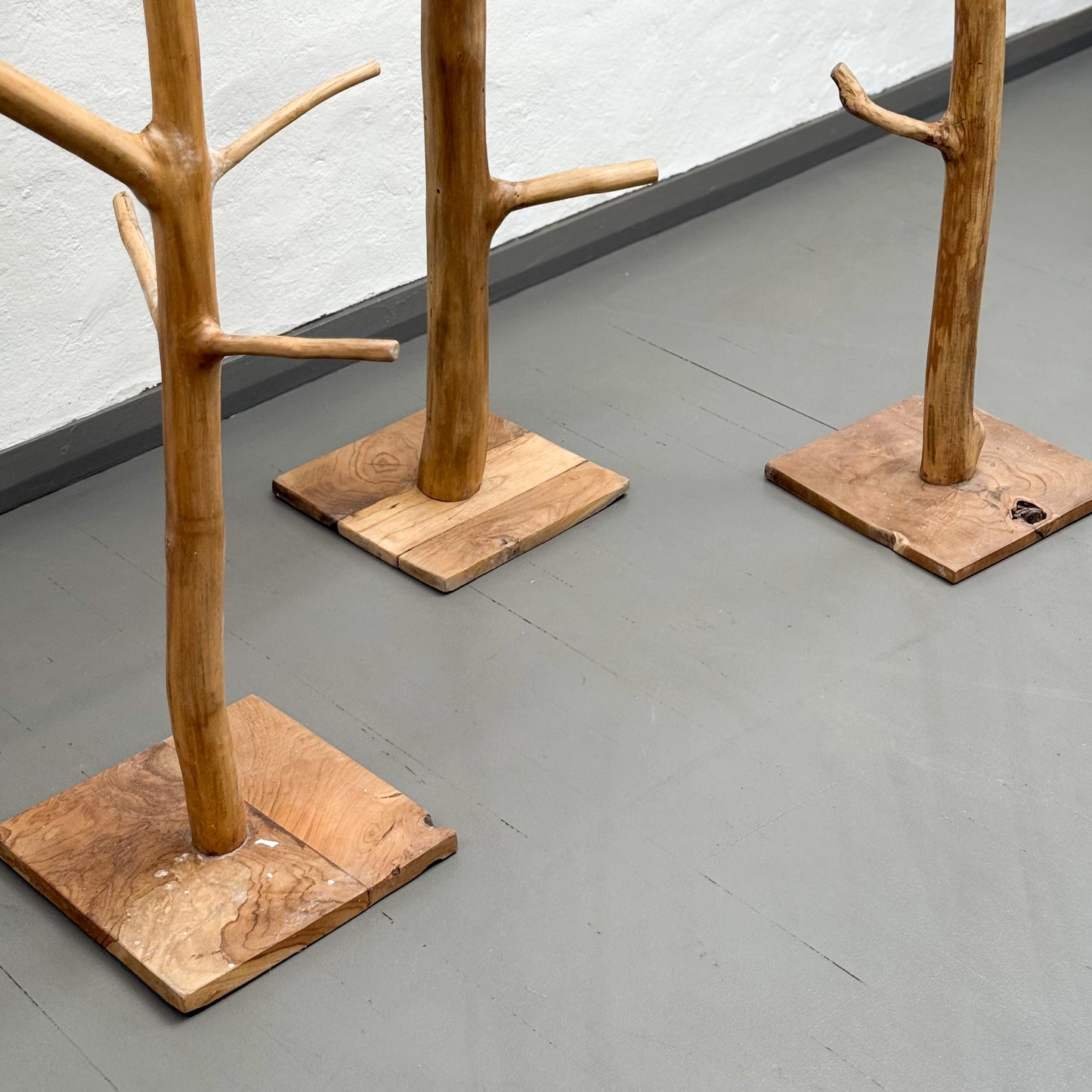 Three wooden coat stands with natural branch designs on a gray floor.
