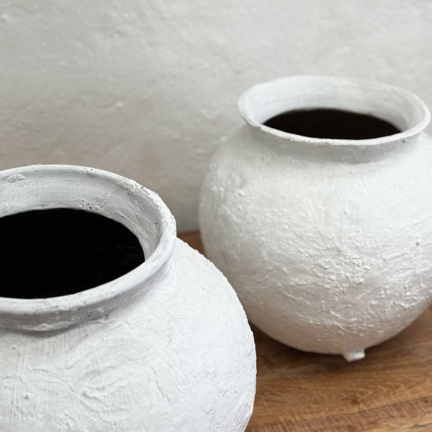 Two white textured pots with dark liquid on a wooden surface and light gray background