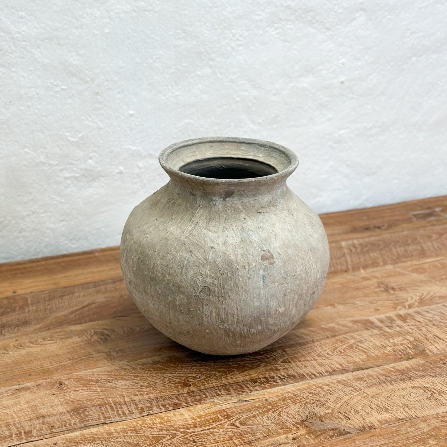 Vintage-style ceramic vase on a wooden surface with a white textured wall background