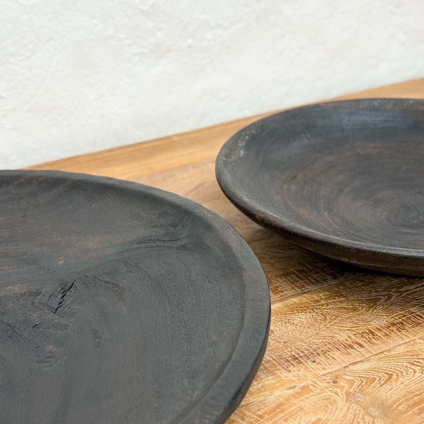 Two black ceramic plates on a wooden surface with a light gray background