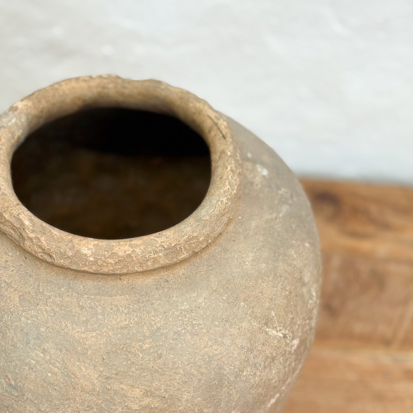 Close-up of a textured clay pot on a wooden surface with a light background