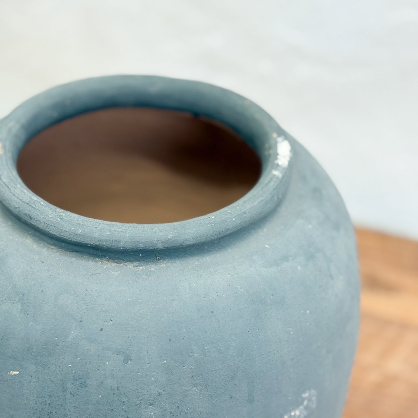 Close-up of a blue ceramic vase on a wooden surface with a blurred background