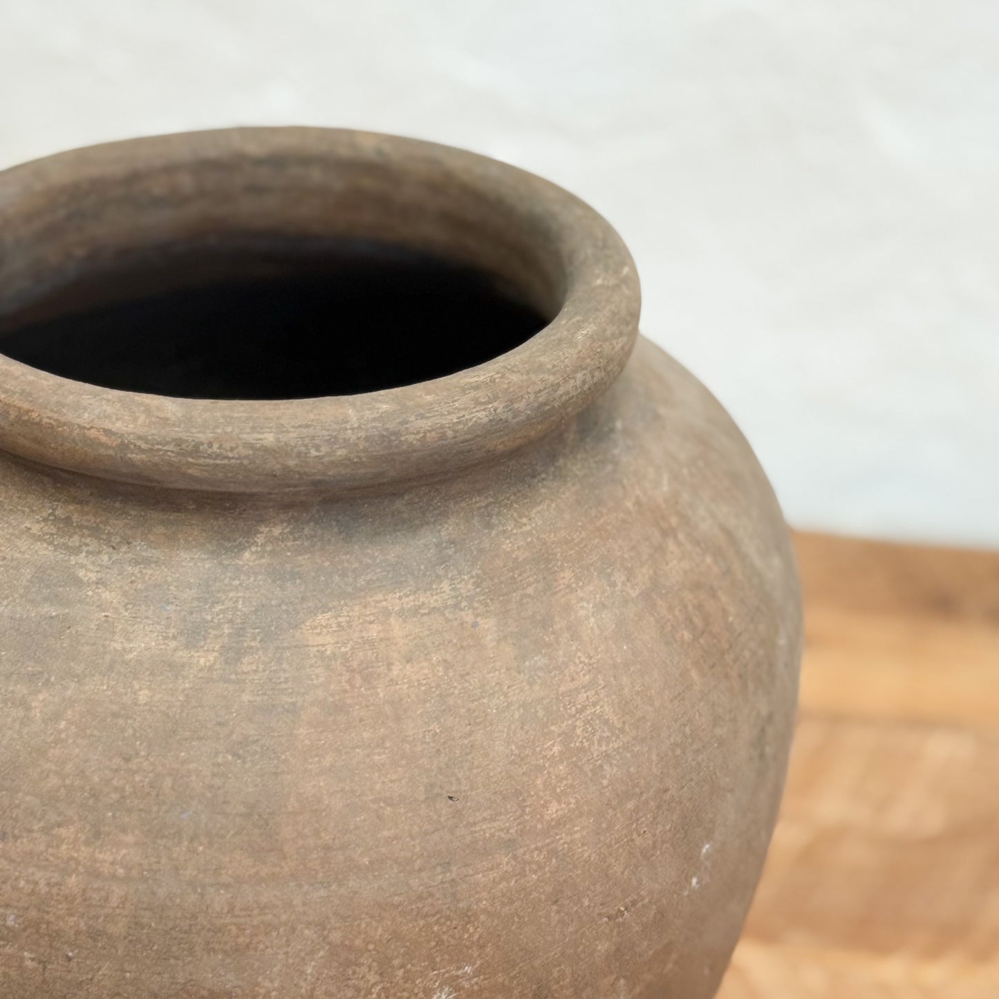 Brown ceramic pot on a wooden surface with a light gray background
