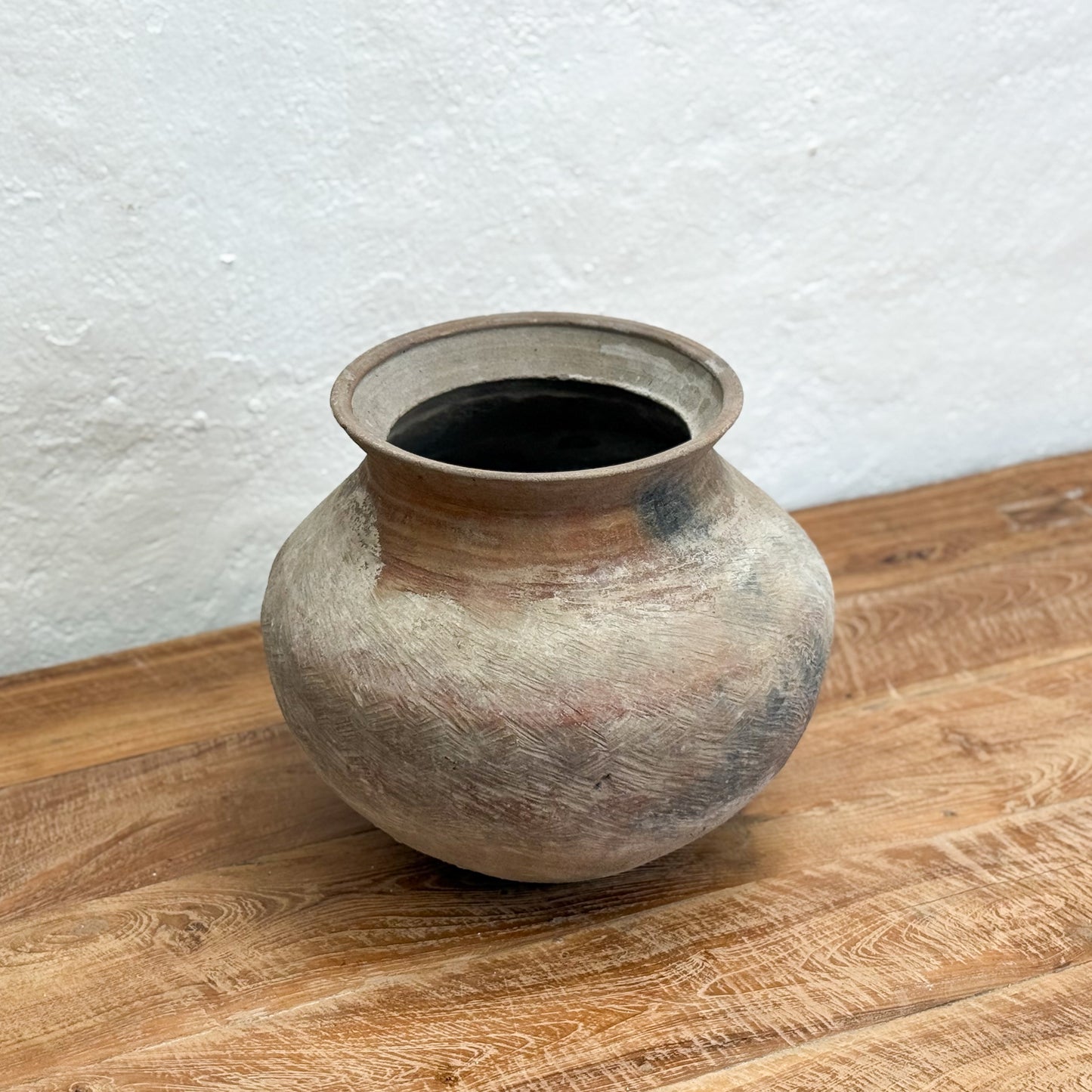 Terracotta pot on a wooden surface with a white textured wall background