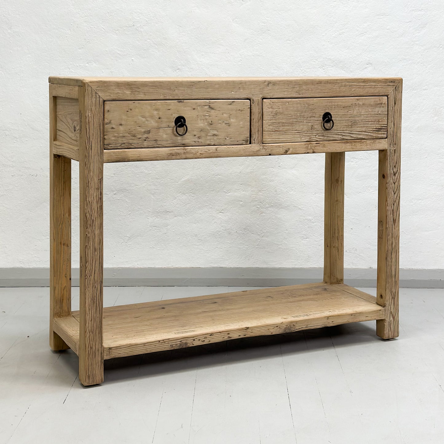 A brown elm wood console table with two drawers and a lower shelf, placed against a plain wall on a white floor.