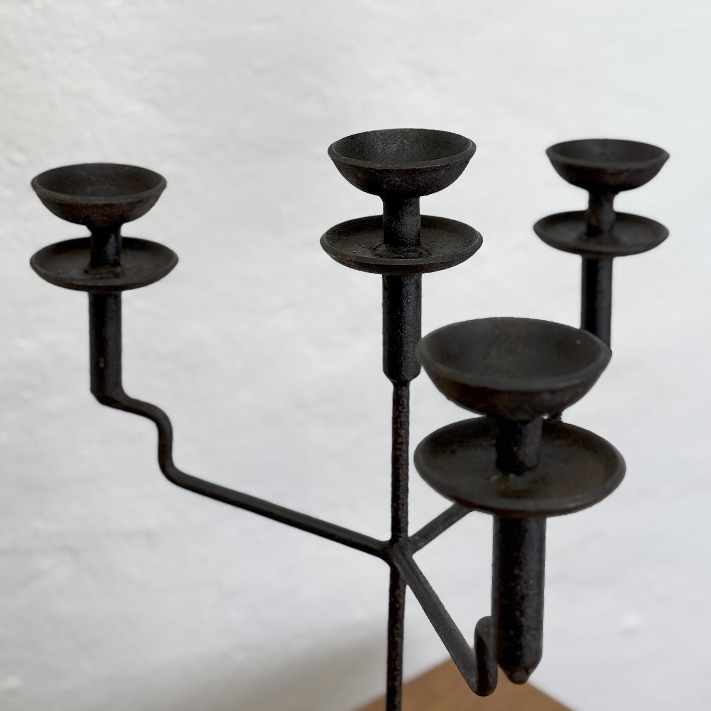A black iron quad candle holder with four cups on a central rod, placed on a wooden surface against a white wall.