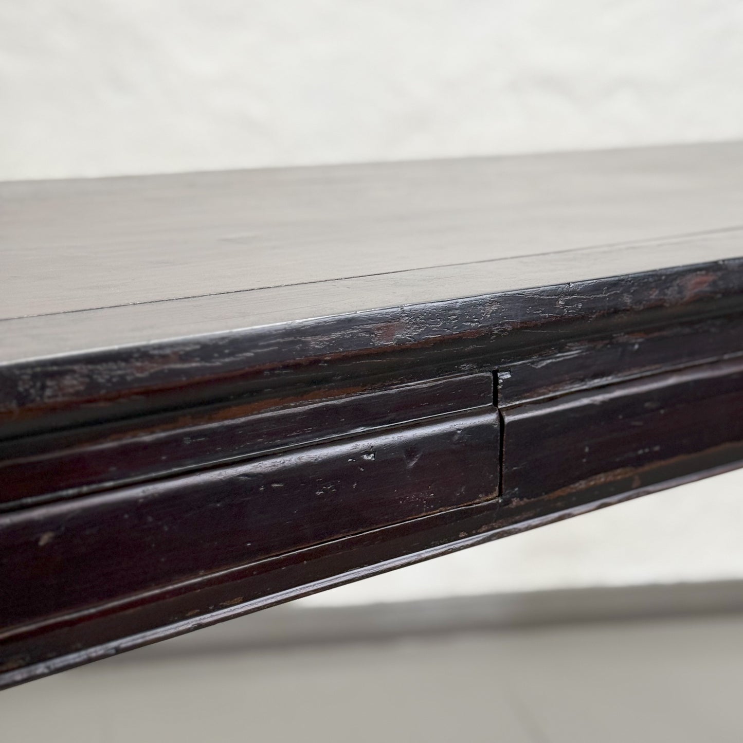 A black vintage Shanxi console table with hidden drawers, placed against a white wall on a neutral surface.