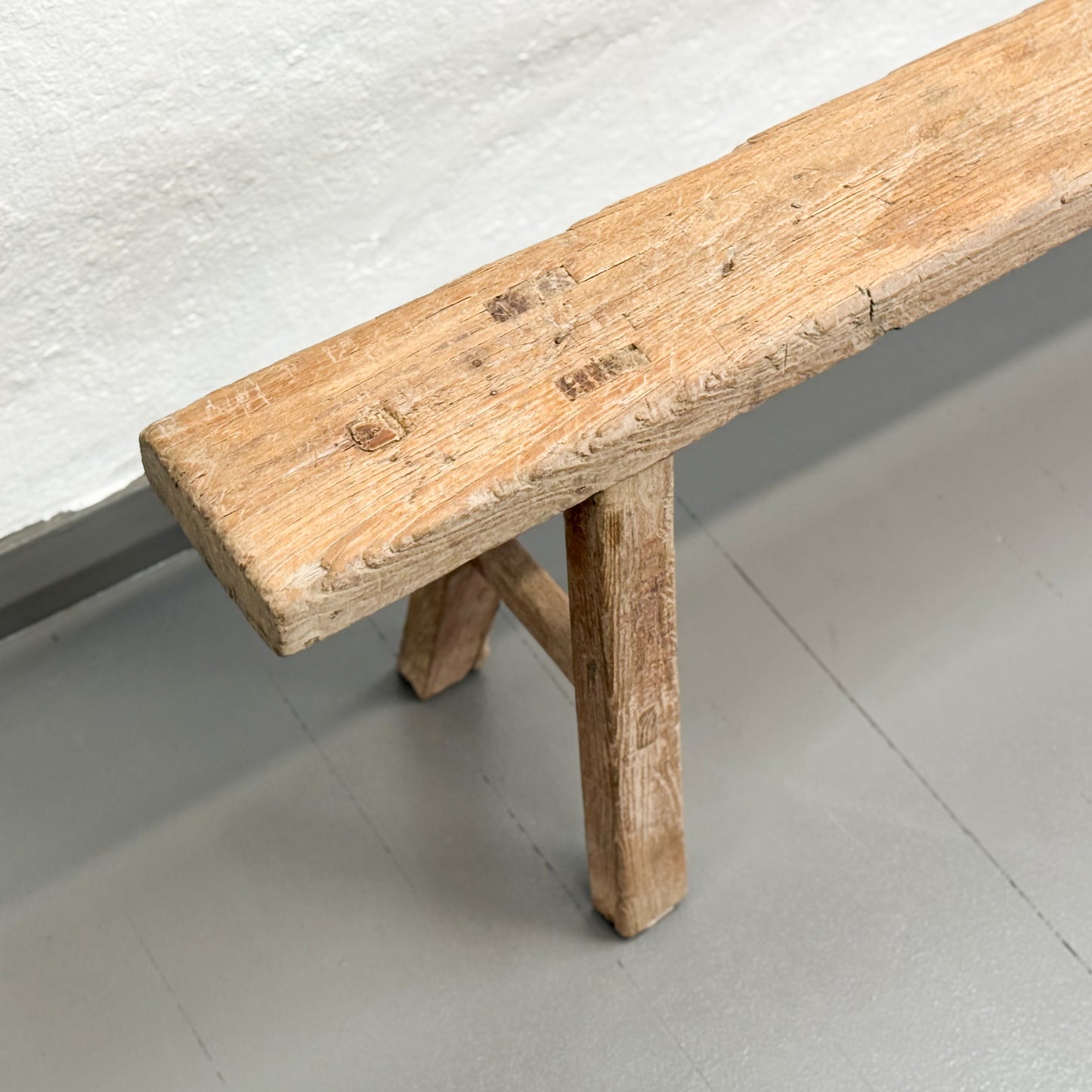 Wooden bench with a textured surface on a light gray floor.