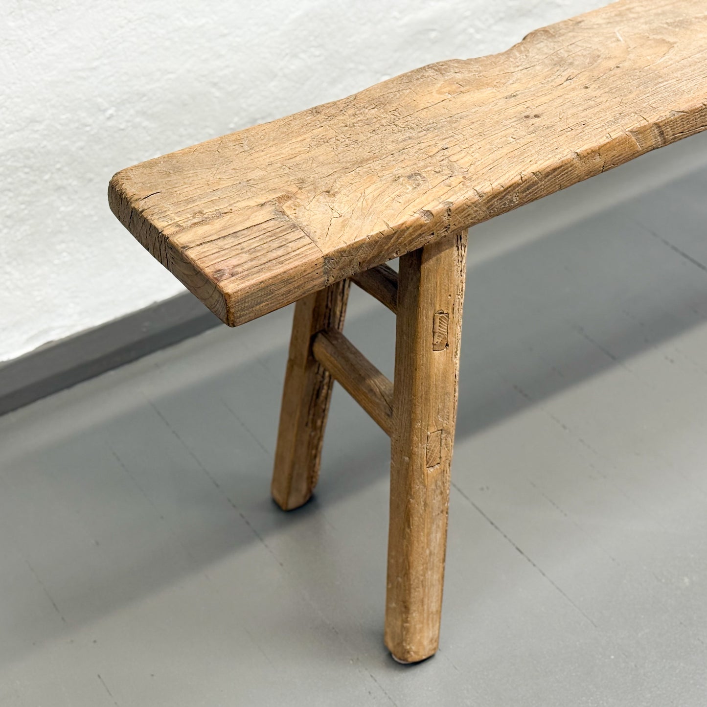 Wooden bench with a rustic design on a light gray floor.